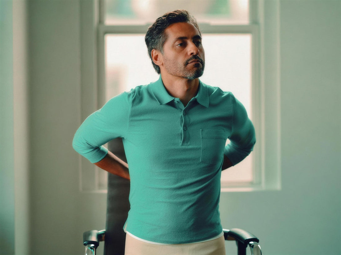 Person in a green shirt standing indoors with their hands behind their back