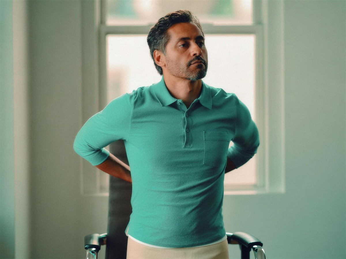 Person in a green shirt standing indoors with their hands behind their back