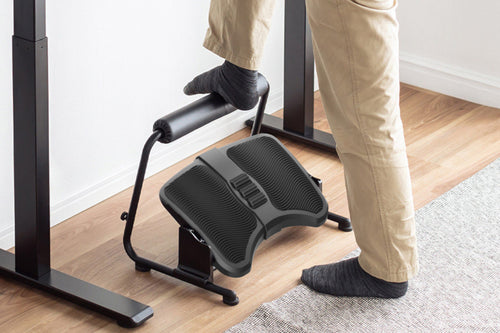 Person standing at a desk with one foot on the Ergoapt Stretch Footrest's padded bar and the other on the floor.