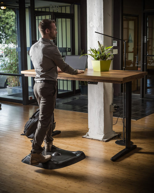 Person standing on a black Topo mat while using a laptop at a standing desk.